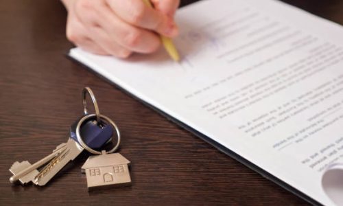 Man client signs new apartment purchase contract with pen near keys with house shaped breloque put on table extreme close view